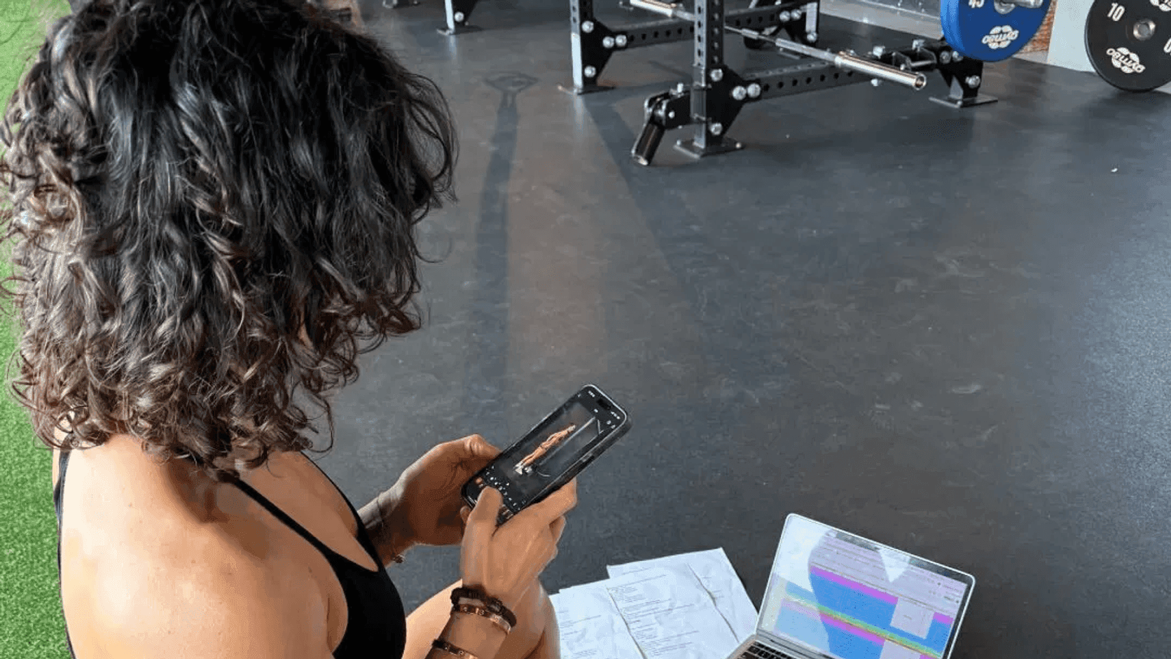 Fitness instructor reviewing class and profile information on a phone and laptop in a gym